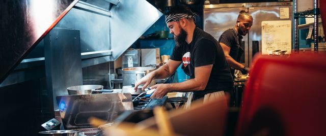 Two chefs work diligently in a bustling restaurant kitchen, preparing meals and managing dishes.