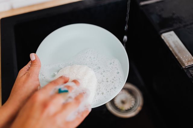 A person washing a plate with soap suds at a kitchen sink, emphasizing cleanliness.